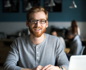 smiling-redhead-man-with-laptop-looking-camera-cafe_1163-5162